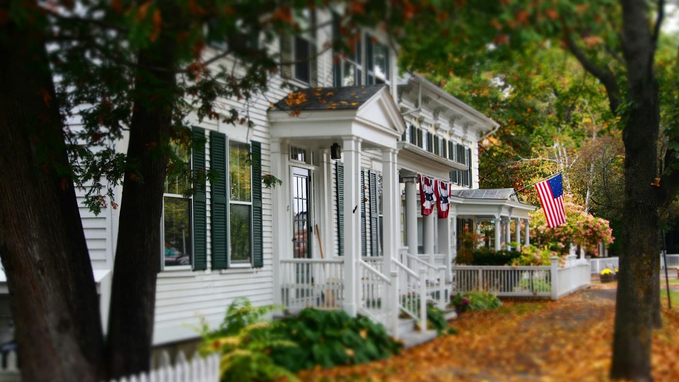 White clapboard New England home with a porch and autumn trees